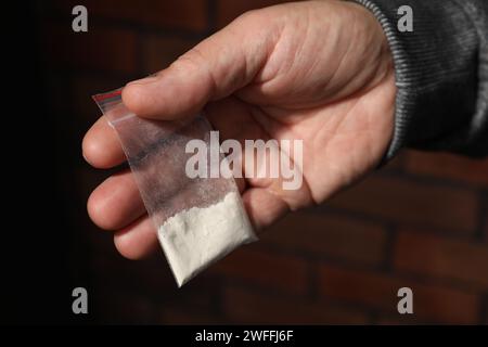 Toxicomanie. Homme avec sac en plastique de cocaïne sur fond flou, gros plan Banque D'Images