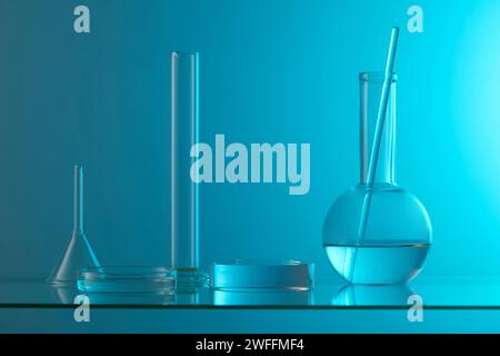 Sur fond bleu, un transparent disposé avec quelques verres de laboratoire sur une table en verre. Vitrine de scène sur l'affichage minimal de podium Banque D'Images