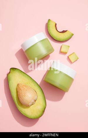 Tranches d'avocat disposées avec deux pots non étiquetés sur fond rose clair pour la promotion du produit de l'extrait d'avocat (Persea americana). Ça aide à renforcer Banque D'Images