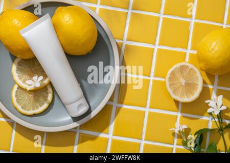 Tube blanc étiquette vide, tranches de citron et petite fleur mis sur un plat rond. Le citron (Citrus limon) peut réduire l'inflammation et la production excessive de sébum. O Banque D'Images