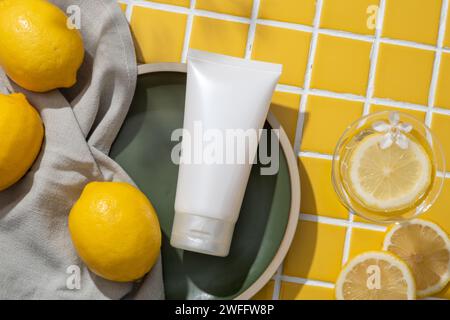 Vue de dessus du récipient cosmétique blanc et une serviette placée sur un plat exposé avec un verre de tranche de citron et fleur blanche. Le citron (Citrus limon) peut obtenir Banque D'Images