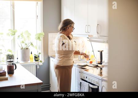 Vue latérale de la femme mature avec handicap préparant le petit déjeuner tout en se tenant dans la cuisine à la maison Banque D'Images