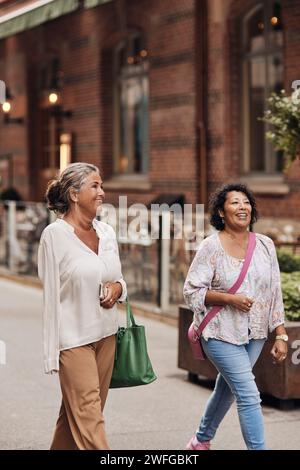 Femme souriante marchant avec une amie handicapée féminine dans la rue Banque D'Images