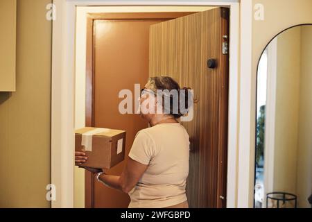 Femme mûre recevant le colis de la personne de livraison à la porte Banque D'Images