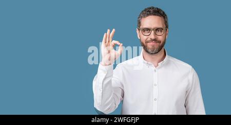 homme regarder dans les lunettes montrer ok isolé sur fond bleu. look homme mûr Banque D'Images