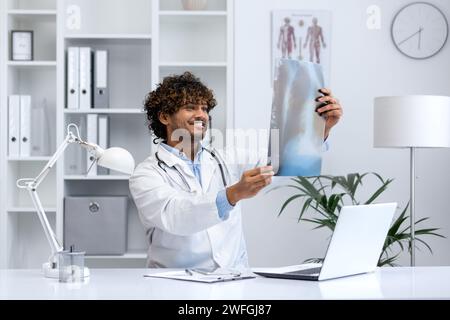 Jeune médecin souriant examinant la radiographie d'un patient dans un cabinet médical moderne et bien éclairé, mettant en valeur son expertise et ses soins. Banque D'Images