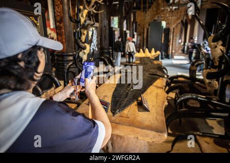 Chiang Rai, Thaïlande. 19 janvier 2024. Un touriste prend une photo de la peau de crocodile à l'intérieur de la Maison Noire. Le «Baan Dam Museum», également connu sous le nom de «Maison Noire» et souvent appelé le «Temple Noir» n'est pas vraiment un temple, mais plutôt un musée d'art et un studio présentant diverses œuvres d'artistes. La «Maison Noire» est également la plus grande collection au monde de restes d'animaux transformés en meubles. Il a été conçu par le célèbre artiste thaïlandais Thawan Duchanee mélangeant des bâtiments traditionnels du nord de la Thaïlande avec une architecture non conventionnelle et contemporaine. Crédit : SOPA Images Limited/Alamy Live News Banque D'Images