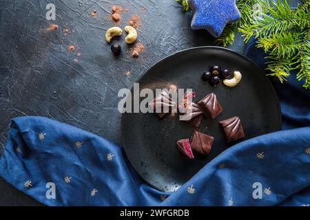 Vue de dessus des barres de bonbons végétaliens au chocolat sur une plaque sombre avec des noix de cajou et des décorations de vacances de Noël autour Banque D'Images