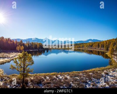 Une superbe prise de vue aérienne capture un lac de montagne serein avec des reflets d'arbres d'automne sous un ciel bleu clair. Banque D'Images