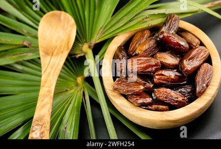 Palmier dattier (Phoenix dactylifera), dattes dans un bol avec feuille de palmier et cuillère en bois Banque D'Images