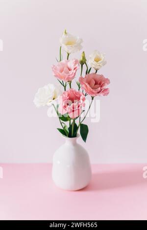 Belles fleurs blanches et roses Eustoma (Lisianthus) dans un vase sur un fond pastel rose. Placer pour le texte. Banque D'Images