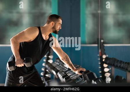 Jeune homme masculin avec barbe et tatouages soulevant des haltères lourds dans la salle de gym Banque D'Images