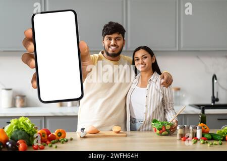 Positif jeune couple indien cuisinant à la maison, montrant le téléphone Banque D'Images