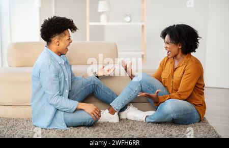 Un jeune couple triste est assis sur le sol ayant une mauvaise conversation, avec des gestes expressifs Banque D'Images