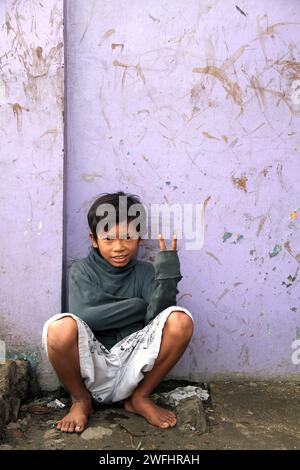 Un enfant de la rue assis contre un mur de couleur violette à Bandung, Java Ouest, Indonésie Banque D'Images