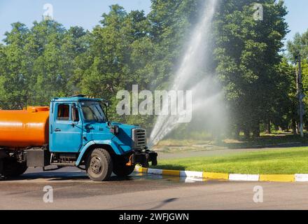 Le camion arrose l'eau sur une pelouse verte dans la ville. Économie urbaine. Amélioration des espaces verts. Banque D'Images