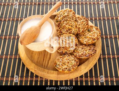 Plusieurs biscuits Thaler avec des noix, du miel et une tasse de crème sure avec un plateau en bois sur un tapis de bambou, macro. Banque D'Images