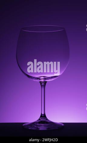 Verre à vin vide sur fond violet. Banque D'Images