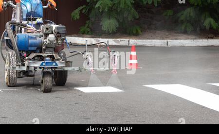 Les travailleurs de la ville peignent les voies de passage sur la route avec la machine à peindre. Banque D'Images