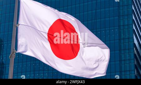 Drapeau japonais brandissant dans une ville moderne de gratte-ciel. Belle grande tour avec bannière japonaise soufflant de la soie douce. Tissu tissu texture ensign fond. S.O. Banque D'Images