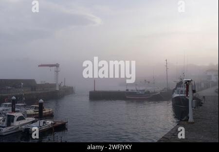 Vue sur le port du village de Comillas en Cantabrie avec beaucoup de brouillard au coucher du soleil. Banque D'Images