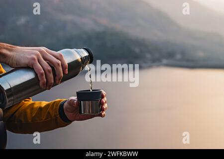 Gros plan de l'homme versant du thé chaud de thermos à l'extérieur avec une belle vue panoramique sur le fond Banque D'Images