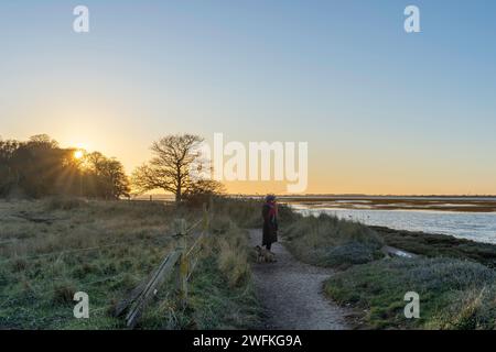 Un observateur avec son chien regardant à travers le magnifique port de Chichester au coucher du soleil depuis le sentier côtier à Itchenor. Banque D'Images