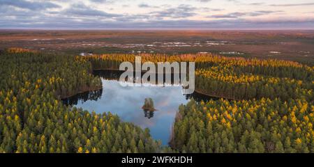 Une vue aérienne sur le lac forestier avec la petite île avec ses pentes esker Hill et fond sauvage de marécages de tourbière illuminés par le soleil. Banque D'Images