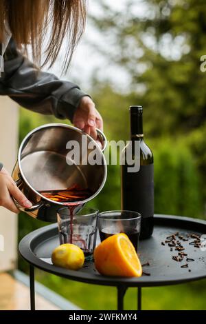 fille verse le vin chaud avec l'ajout d'épices et d'agrumes dans un pot sur une table en bois rustique, vue de dessus. Pot de vin chaud, chri traditionnel Banque D'Images