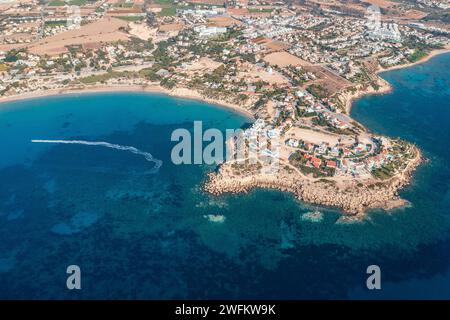 Vue aérienne de haut en bas du village pittoresque niché par la côte chypriote, avec des eaux azur et des bateaux parsemant le paysage marin. Banque D'Images