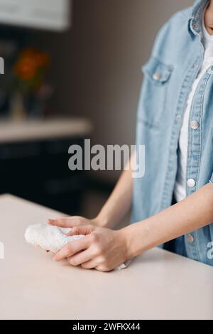 Femme au foyer nettoyage Table de cuisine avec farine et pâte, gros plan des mains de femme travaillant avec du pain maison Banque D'Images