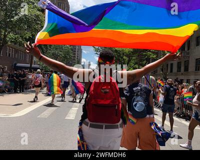 Un jeune homme hisse le drapeau arc-en-ciel de la fierté au-dessus de sa tête alors qu'il marche dans la parade de la fierté de New York célébrant la communauté LBGT Banque D'Images