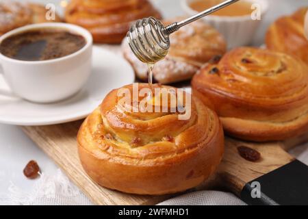 Verser du miel sur de délicieux rouleaux avec des raisins secs à table, gros plan. Petits pains sucrés Banque D'Images