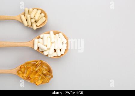 Cuillères en bois avec différentes capsules de vitamines sur fond gris clair, pose plate Banque D'Images