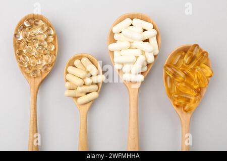 Cuillères en bois avec différentes capsules de vitamines sur fond gris clair, pose plate Banque D'Images