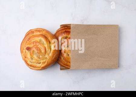 Sac en papier avec de délicieux rouleaux sur la table en marbre blanc, vue de dessus. Petits pains sucrés Banque D'Images