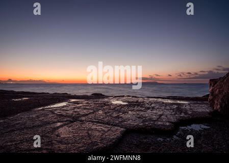 Mer lisse au crépuscule - prise de vue longue exposition avec vagues floues. Rochers mouillés sur la côte de la mer après le coucher du soleil. Banque D'Images