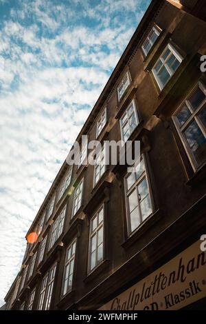 vieux bâtiment brun dans les rayons du soleil de l'après-midi. Façade d'un bâtiment du 18ème siècle avec beaucoup de fenêtres ; ciel jonché de minuscules nuages Banque D'Images