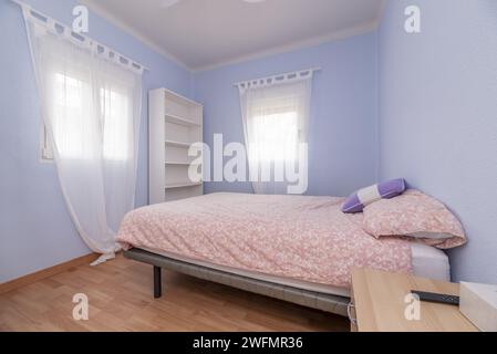 Une chambre double avec des murs bleu pâle et des rideaux blancs translucides sur les fenêtres Banque D'Images