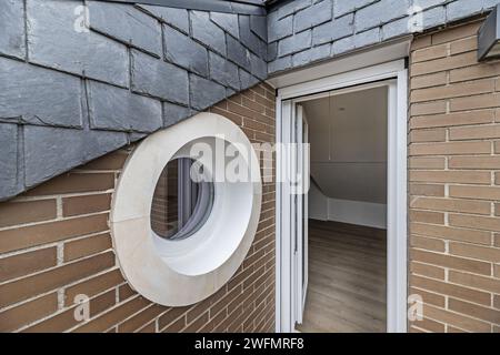 Petite terrasse d'une maison résidentielle avec des toits en ardoise noire, une fenêtre de style hublot avec maçonnerie extérieure décorative. Banque D'Images