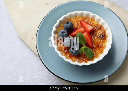 Délicieuse crème brulée avec des baies et de la menthe dans un bol sur une table texturée grise, vue au-dessus Banque D'Images