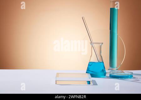 Un erlenmeyer avec une tige en verre à l'intérieur, un tube à essai et une boîte de Pétri remplie de liquide bleu. Podium transparent rectangle avec espace vide pour la production Banque D'Images