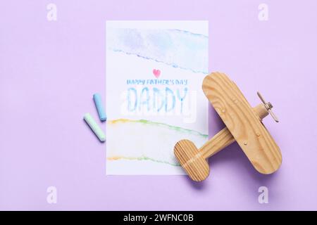 Carte pour la fête des pères avec craies et avion en bois sur fond lilas Banque D'Images