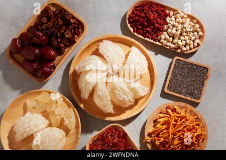 Un plat en bois de nid d'oiseau comestible exposé avec des baies de goji séchées, des graines de lotus, des graines de chia, des cordyceps et d'autres herbes. Les herbes et le nid d'oiseau ont un lo Banque D'Images