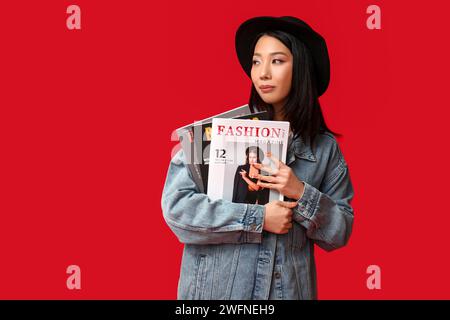 Belle jeune femme asiatique dans une veste en denim élégante avec magazine sur fond rouge Banque D'Images