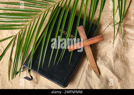 Croix en bois avec feuille de palmier et Sainte Bible sur sable Banque D'Images