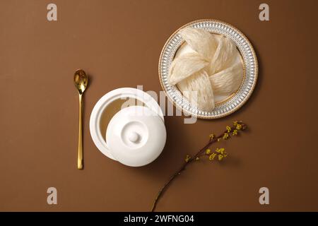 Un bol contenant de la soupe de nid d’oiseau décoré d’un plat de nid d’oiseau comestible et de branche de fleur sur fond brun. Le nid d’oiseau peut aider les gens à traîner Banque D'Images