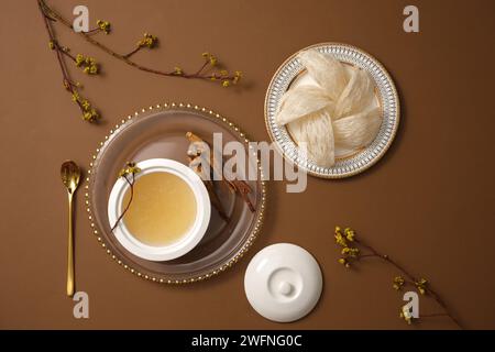 Un plat avec un nid d’oiseau comestible placé et un bol de soupe de nid d’oiseau exposé avec du ginseng (Panax ginseng) sur fond brun. Ginseng et Bird’s ne Banque D'Images