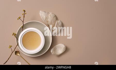 Un bol en porcelaine blanche placé sur un plat avec un nid d’oiseau comestible à côté de lui et une cuillère avec une branche de fleur. Espace vide pour la promotion des produits. Bird’s n Banque D'Images