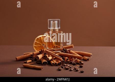 Une bouteille transparente en verre remplie de parfum extrait de grains de café, de bâtonnets de cannelle et de tranche d'orange séchée, affichée sur fond minimaliste foncé Banque D'Images